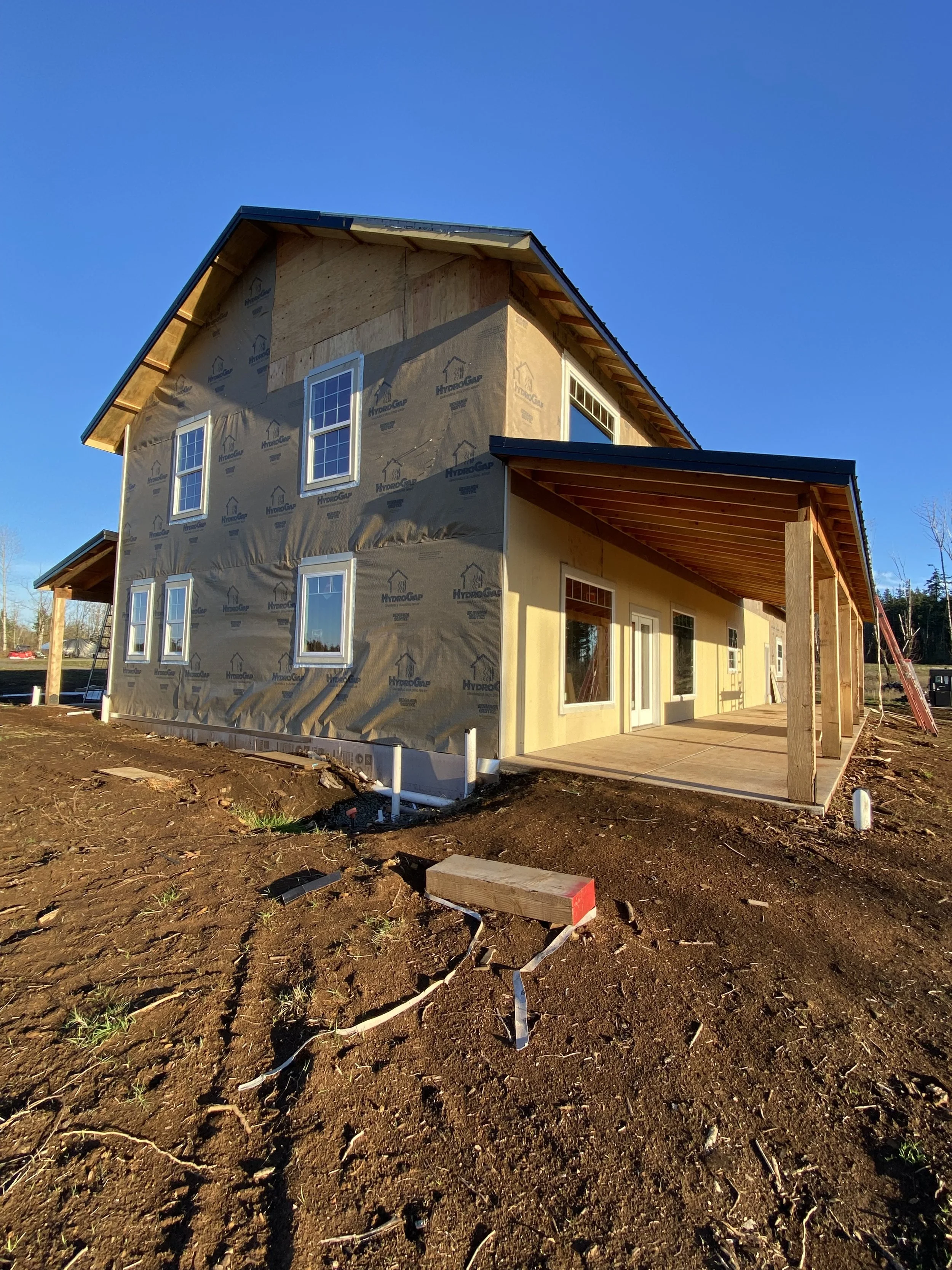A two-story house under construction with exterior sheathing and windows, a covered porch, and a clear blue sky.
