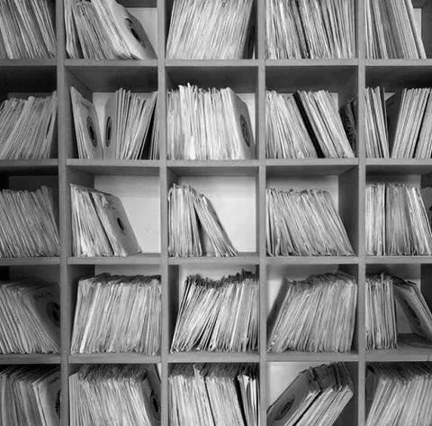 A bookshelf filled with disorganized files and papers in a grid of cubbyholes.