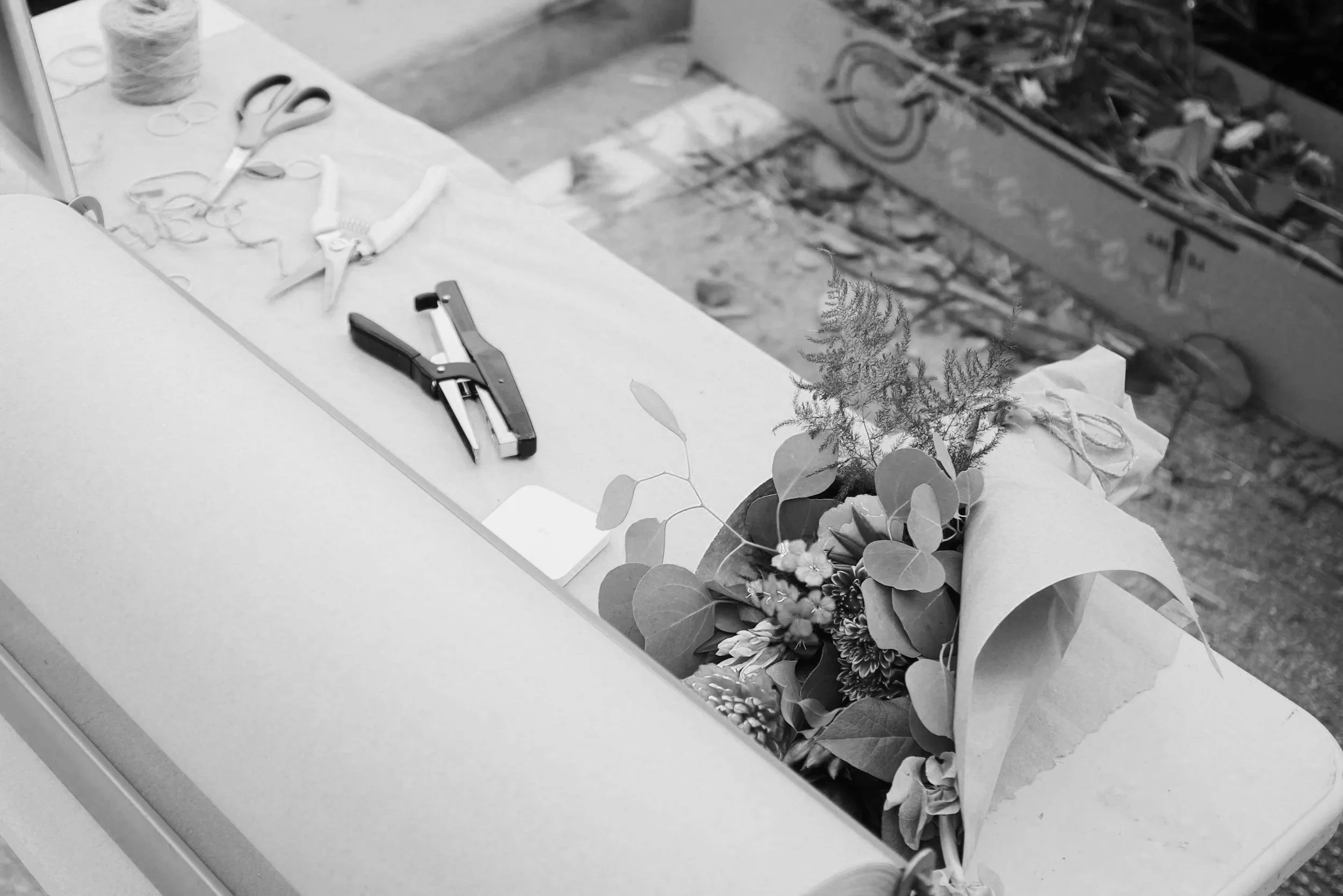 A workspace with flower arrangements, scissors, a stapler, and other tools on a table, with a floral pattern in the background.