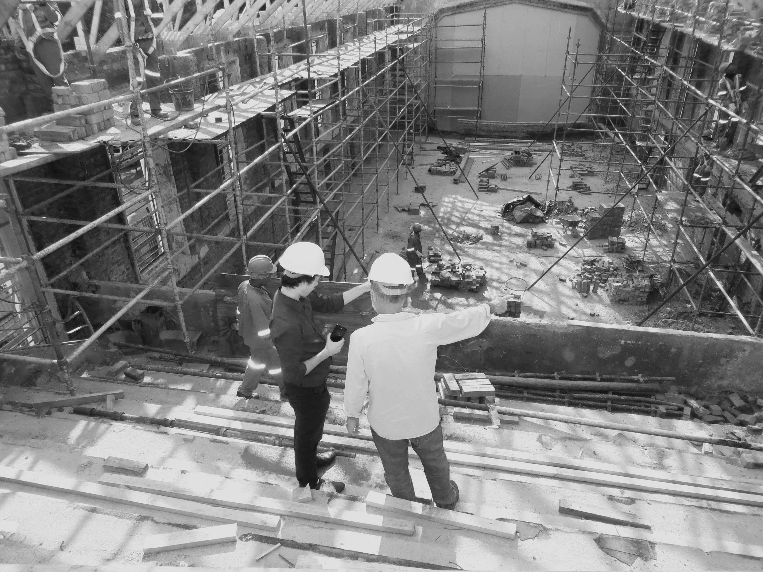 Construction site with workers wearing helmets, scaffolding, and building materials, viewed from above.