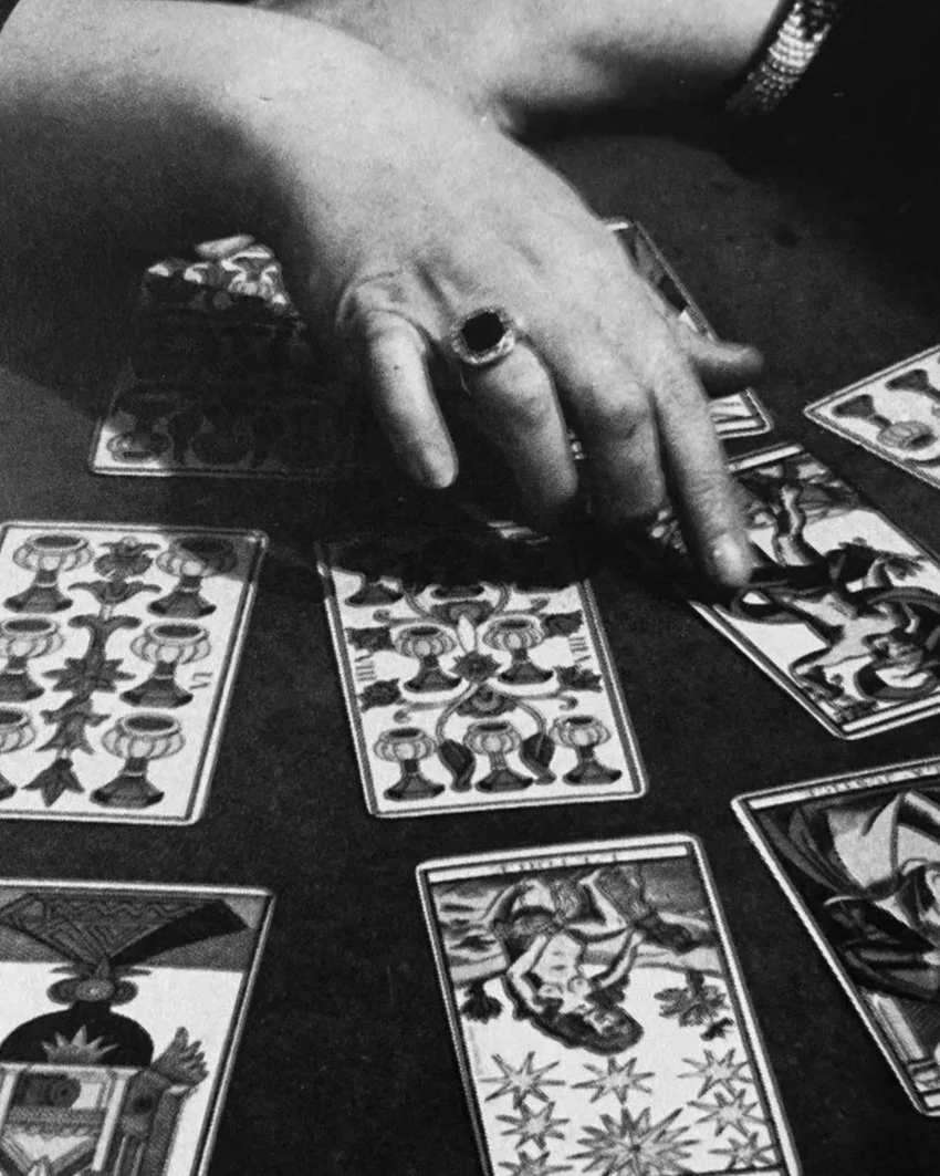 A person's hand with rings placed on a table with various tarot or oracle cards spread out.