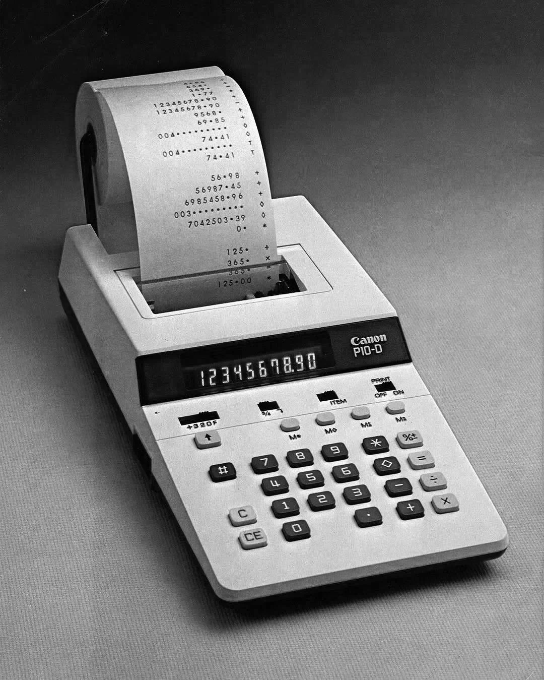 A black and white image of a Canon PIO-D printing calculator with a printed receipt showing numbers and calculations.