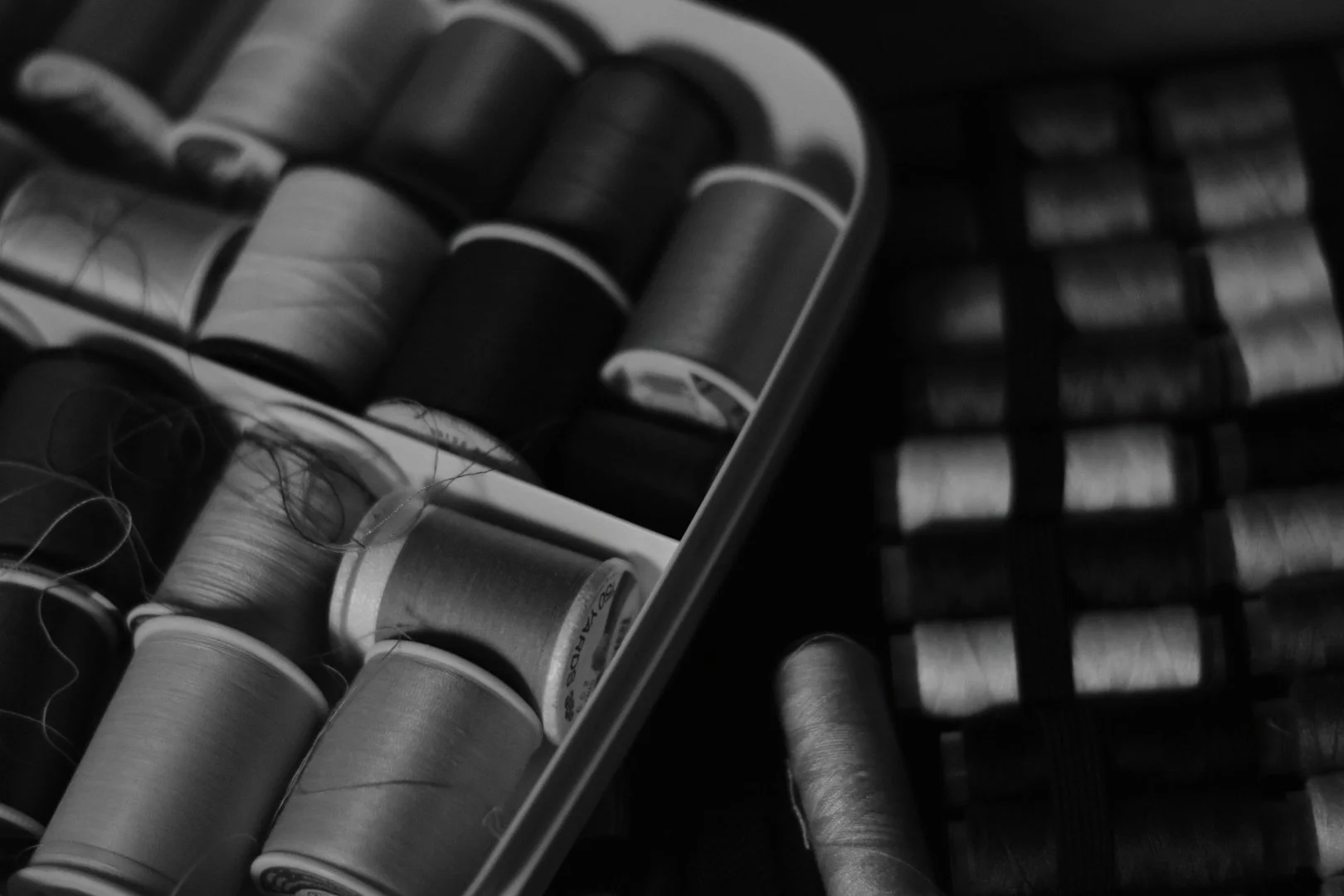 Close-up black and white photo of spools of embroidery thread in a drawer.