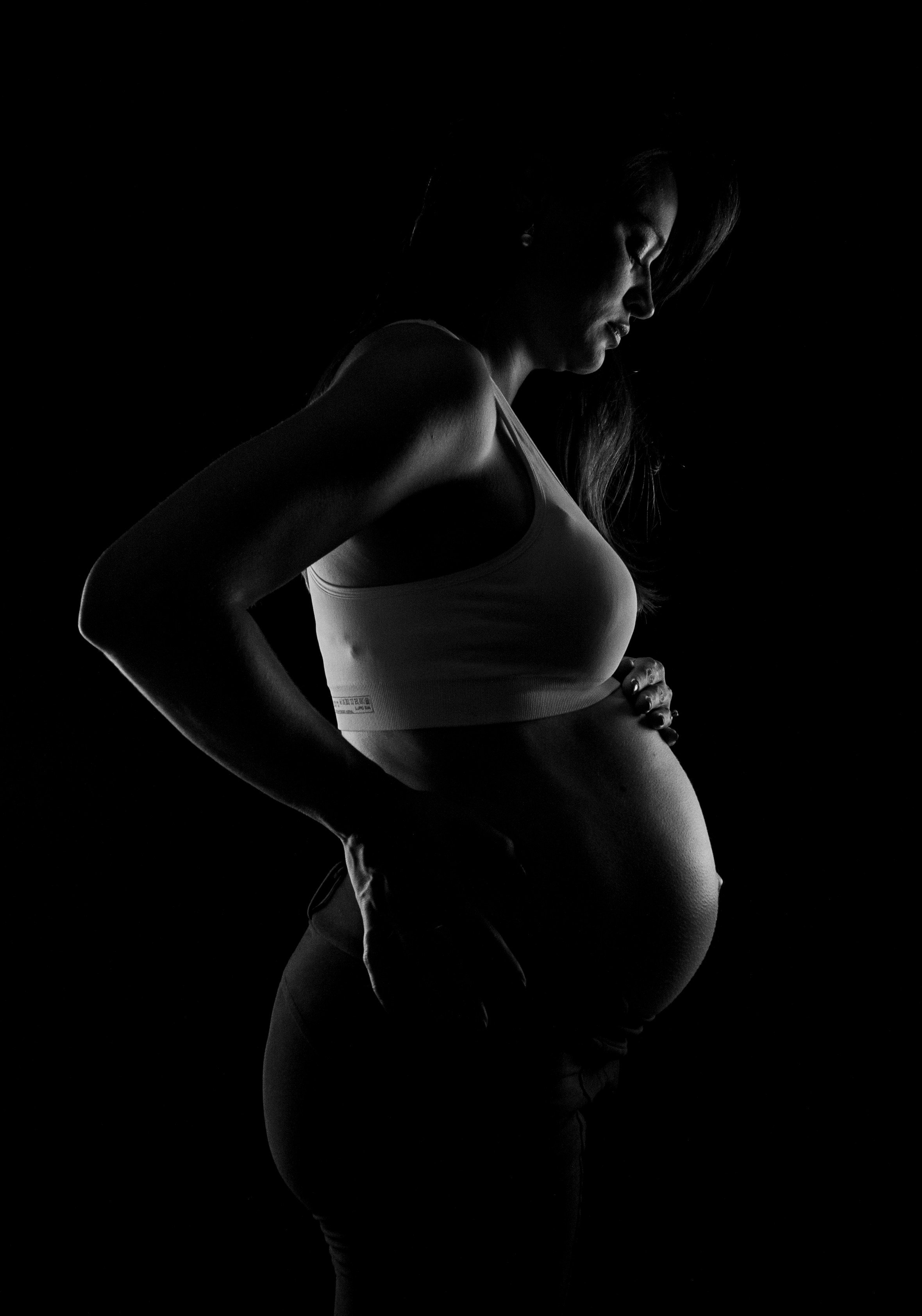Silhouette of a pregnant woman with her hand on her belly, facing sideways in a dark background.