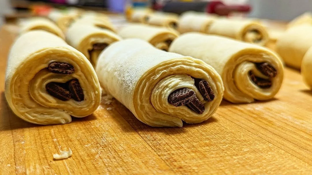 Raw puff pastry rolls filled with chocolate chips, arranged on a wooden surface.