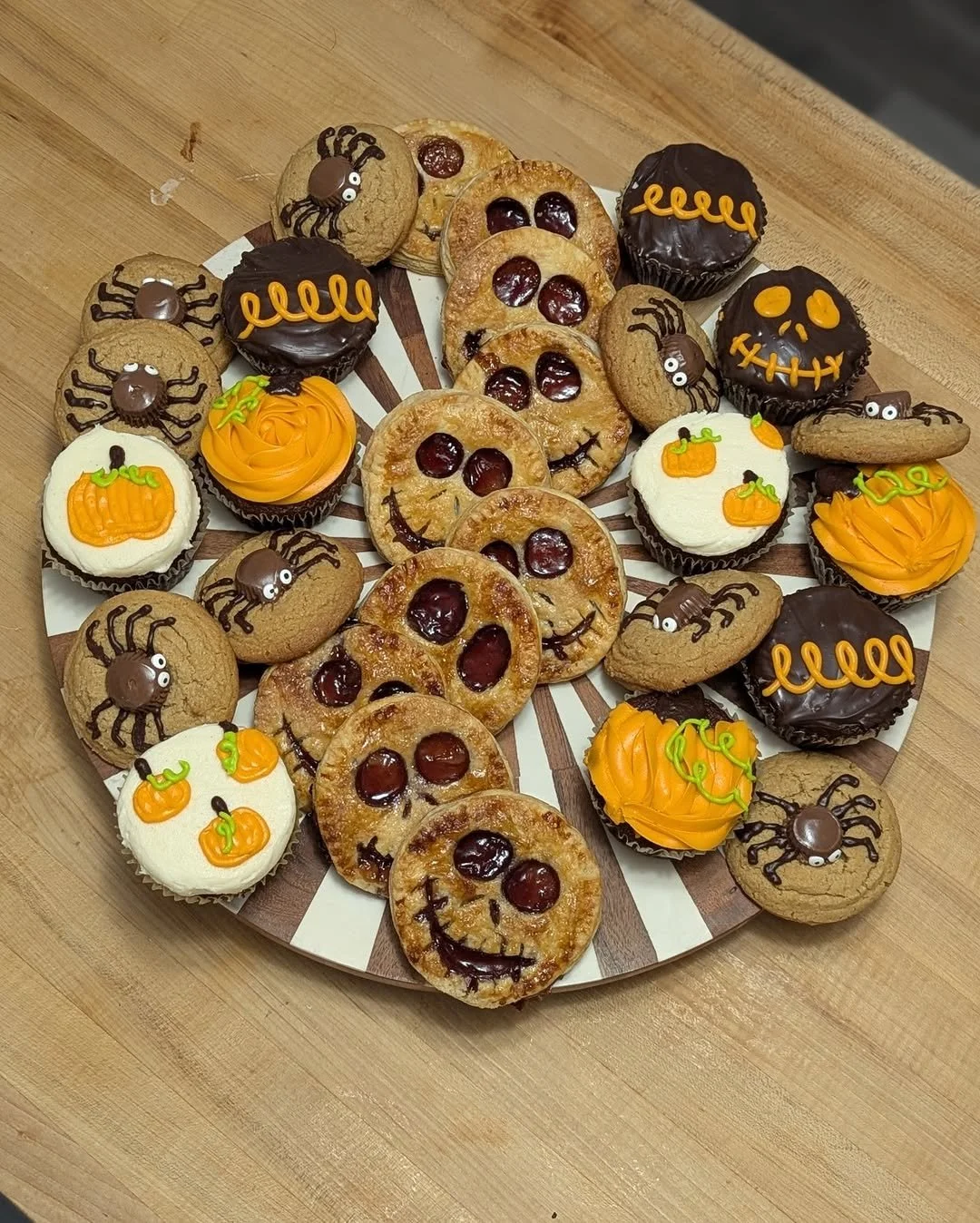 A plate of Halloween-themed cookies and cupcakes decorated with pumpkins, spiders, and smiling faces.