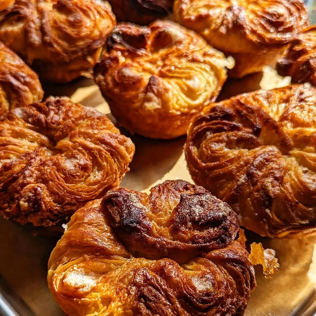 Close-up of several golden-brown fried pastries with flaky, crispy layers on a baking sheet.