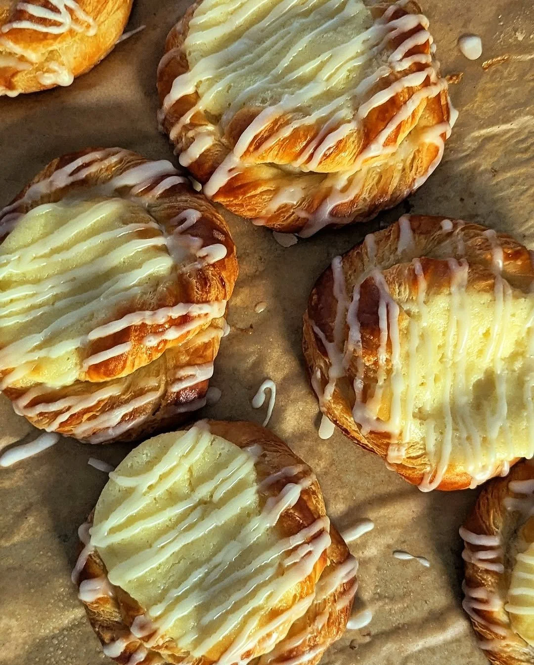 Close-up of apple pastries topped with white icing drizzle on parchment paper.
