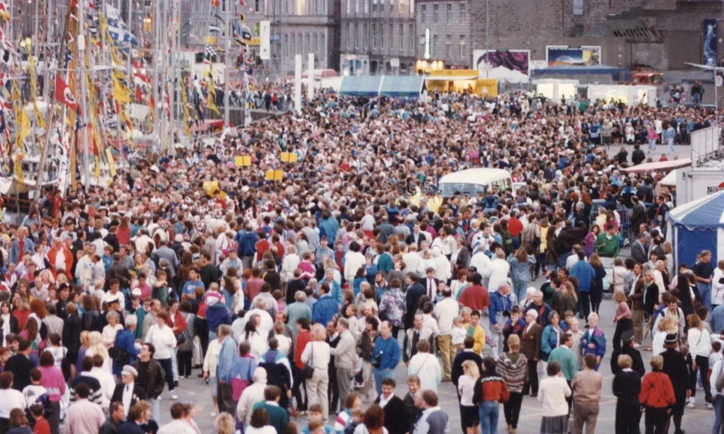 A crowded outdoor festival with numerous people walking around, fair booths, and rides.