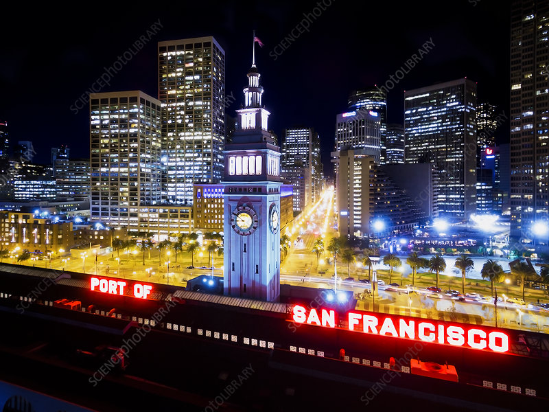 Night view of Downtown San Francisco with a clock tower in the foreground and illuminated city skyscrapers in the background, including a sign reading "Port of San Francisco."