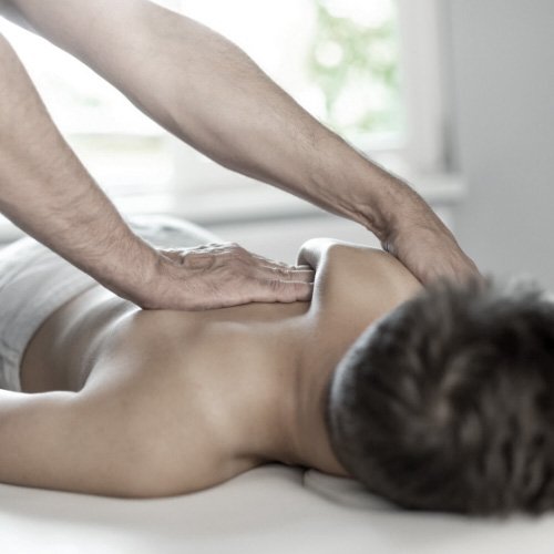 Person receiving a massage on their back from a massage therapist in a bright room.