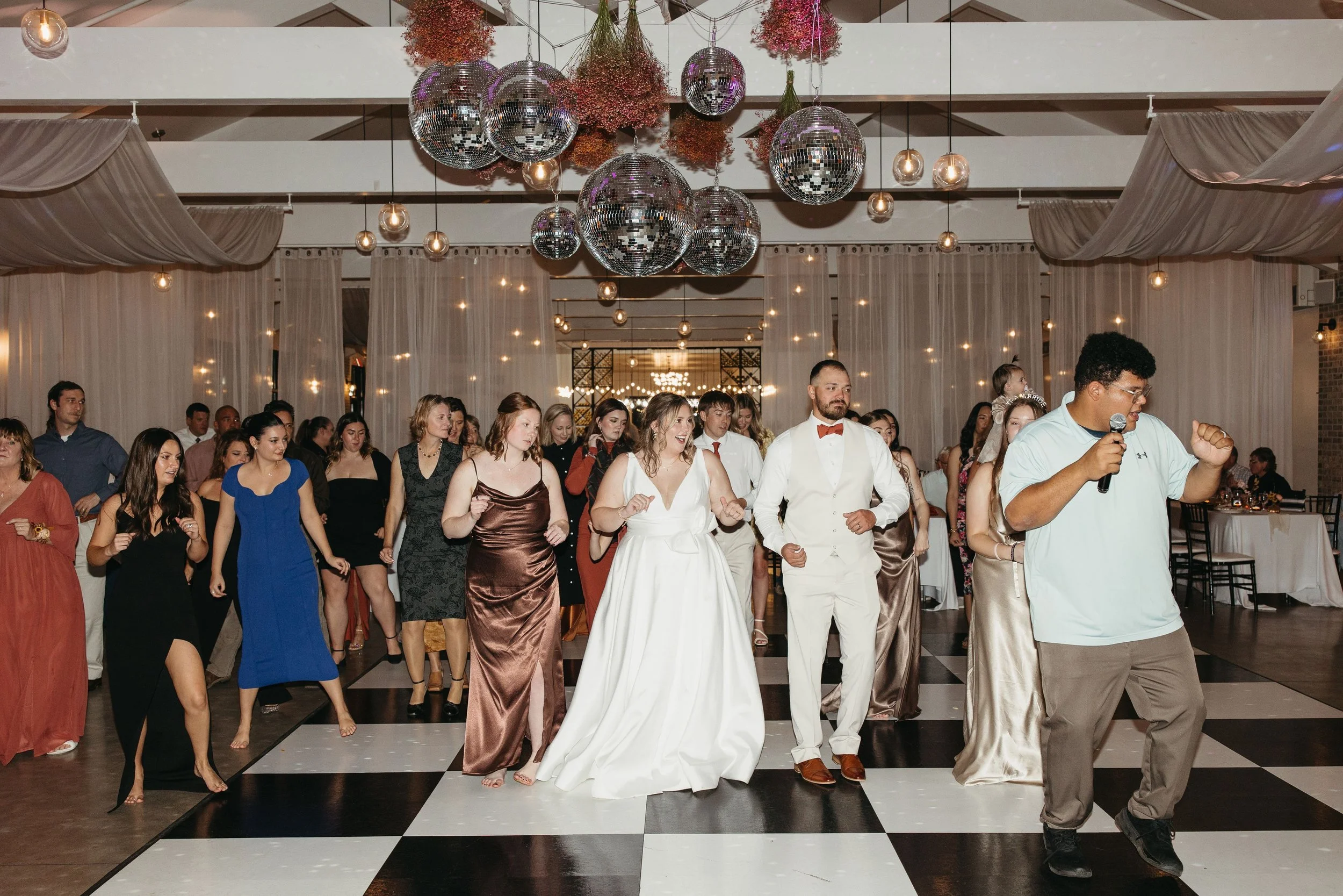 People dancing at a wedding reception under disco balls and string lights.
