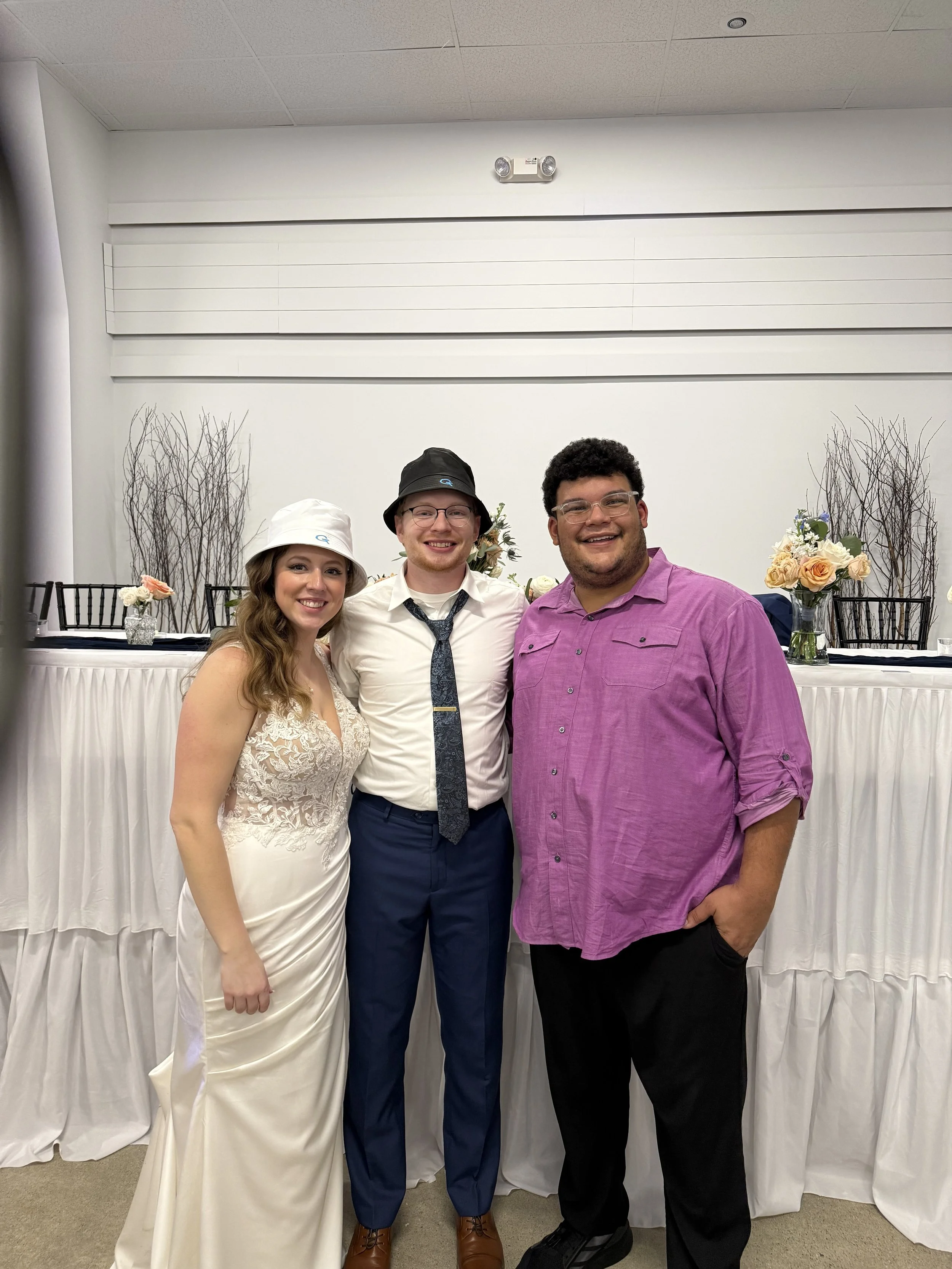 Three people standing together in front of a decorated table at a celebration or event, smiling and posing for the photo.