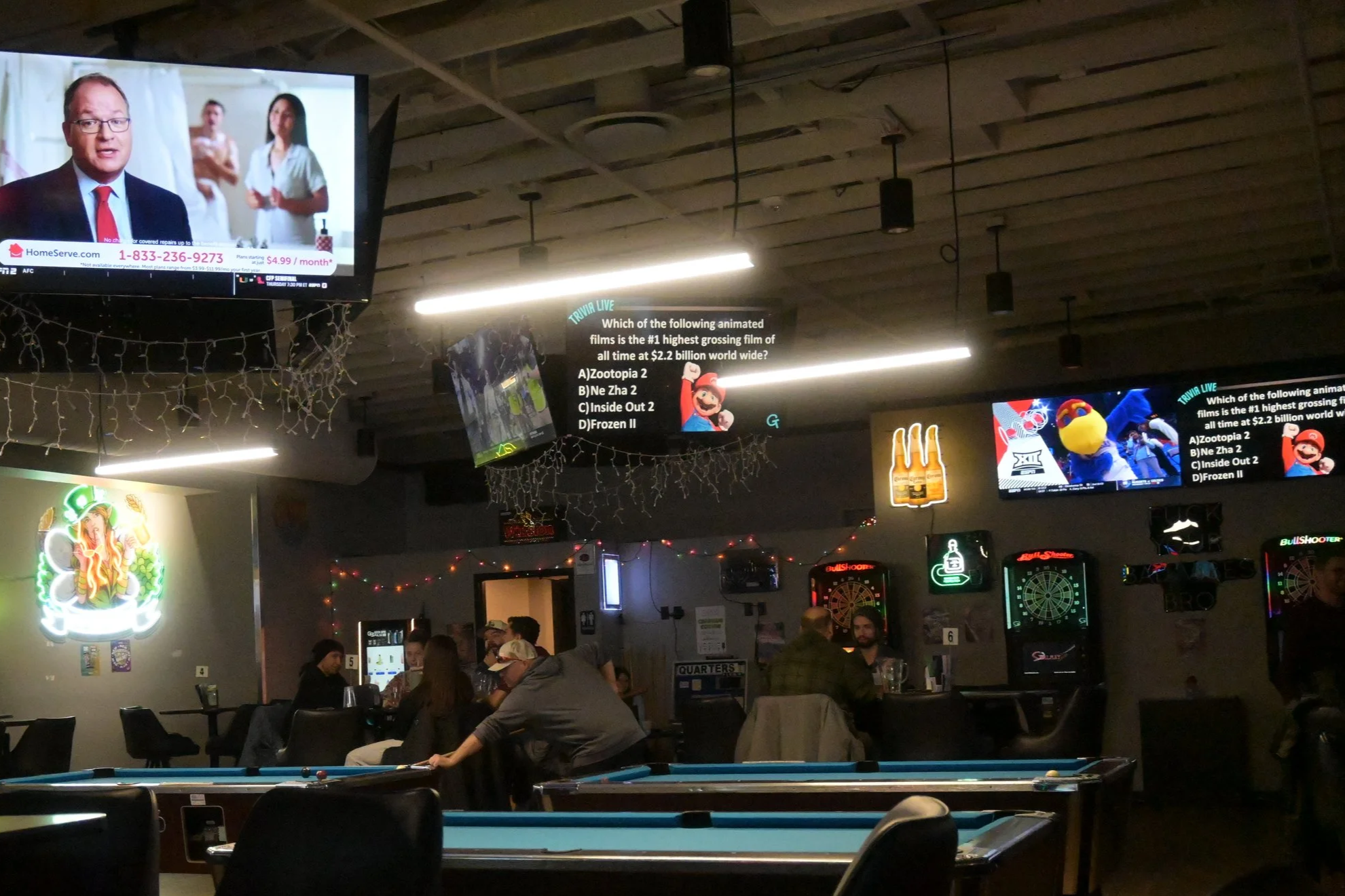 Crowded bar or restaurant with groups of people sitting at tables, watching TV screens on the wall, and playing Good Times Live Trivia.