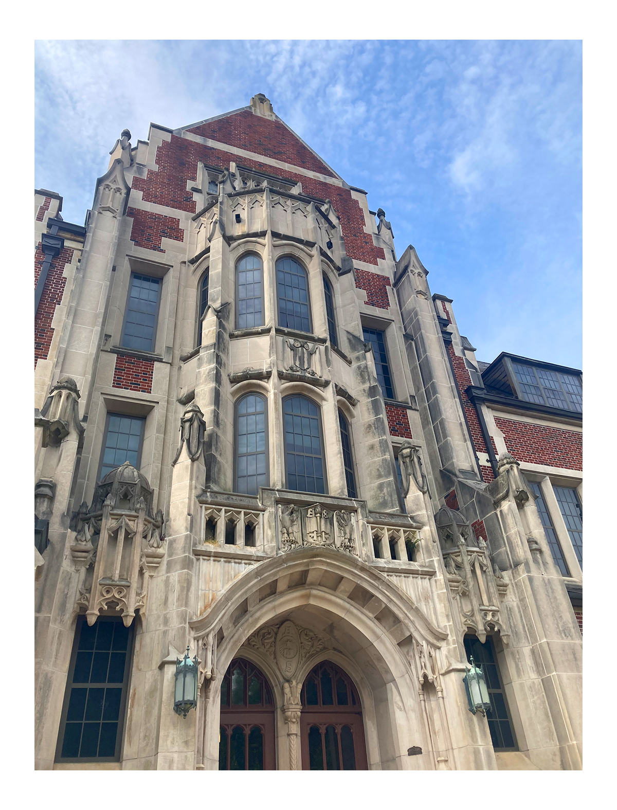 A Gothic-style castle building with ornate stonework, stained glass windows, and a large arched entrance, set against a blue sky with some clouds.