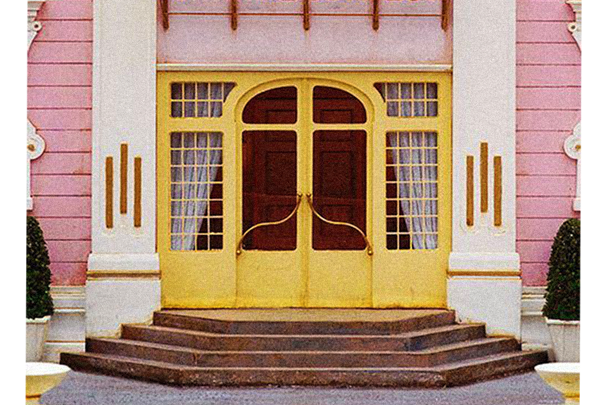 Pink and white Victorian-style building with yellow double doors, steps, and decorative trim.