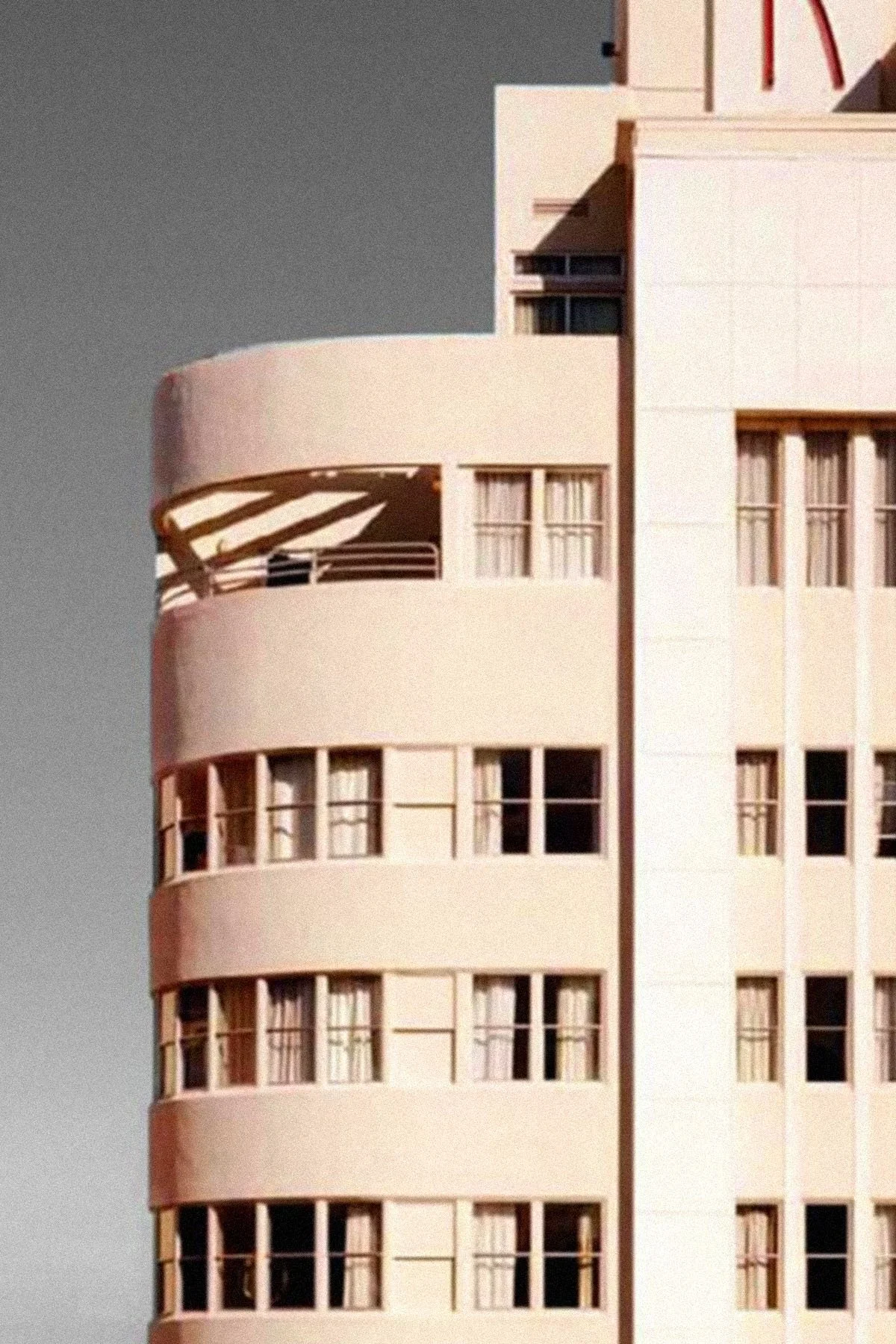 A high-rise building with rounded balconies and large windows, some with curtains, against a dark sky.
