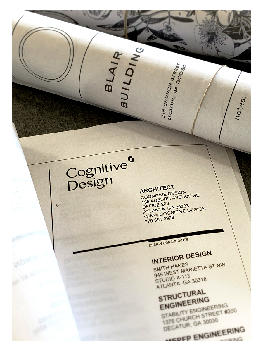 Architecture and design plans including a rolled-up blueprint labeled 'Blair Building' and a printed sheet titled 'Cognitive Design' with contact information for architect, interior designer, and structural engineer.