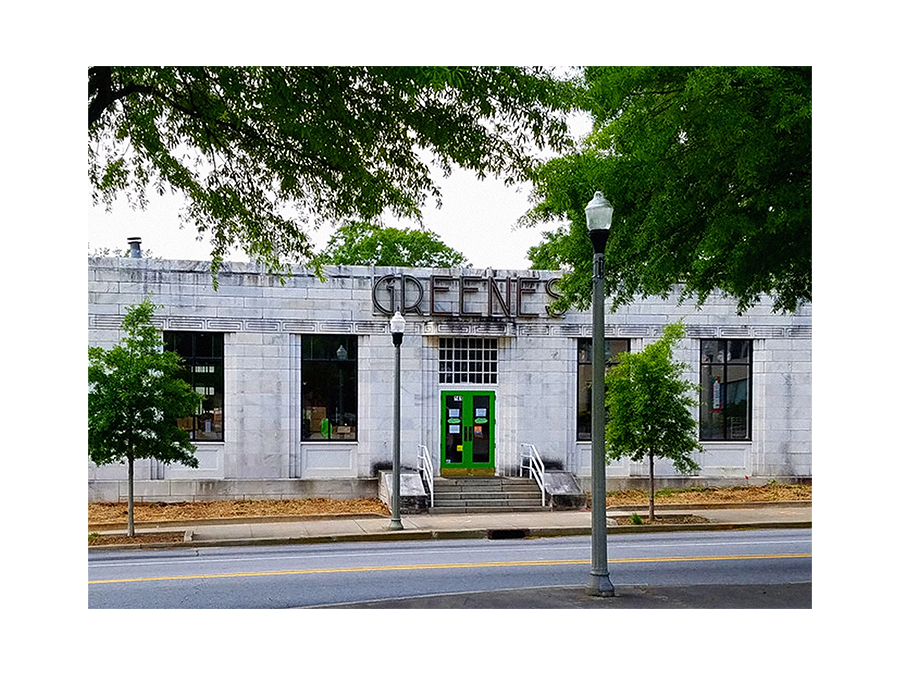 A gray brick theater building with large windows, green doors, and a sign that reads 'CRENES' partially obscured. Two trees and streetlights are in front of the building, and the street has visible yellow dividing lines.