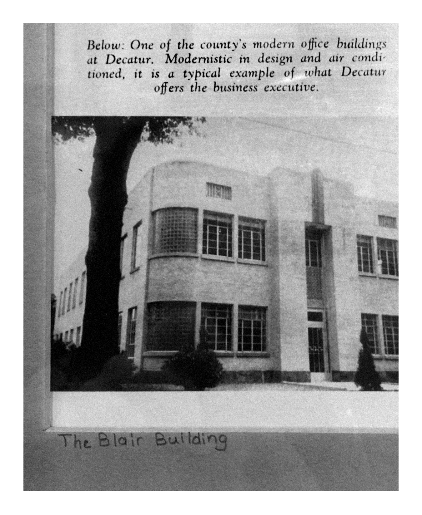 Black and white photograph of the Blair Building, a modern office building with multiple windows, surrounded by trees, with a handwritten caption below that reads "The Blair Building".