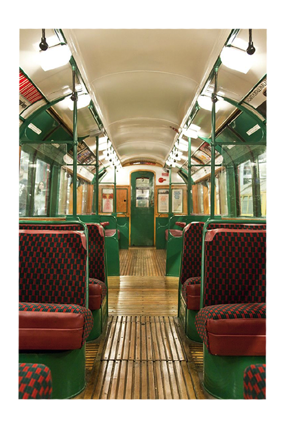 Interior of a vintage train carriage with green walls, red and black plaid patterned seats, wood flooring, and overhead lighting.