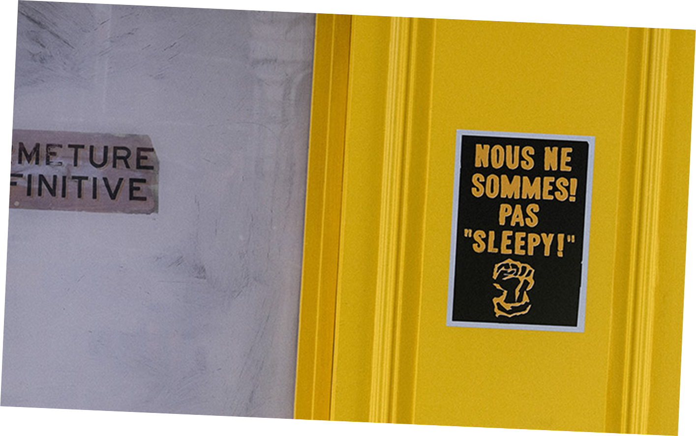 Yellow door with a black and yellow poster that reads 'We are not asleep!' and includes an illustration of a fist