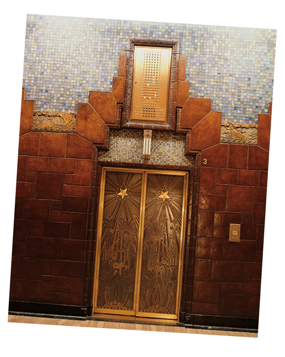 Elevator with decorative gold doors featuring stars and intricate patterns, set in a wall with brown tiles and blue mosaic tiles above.