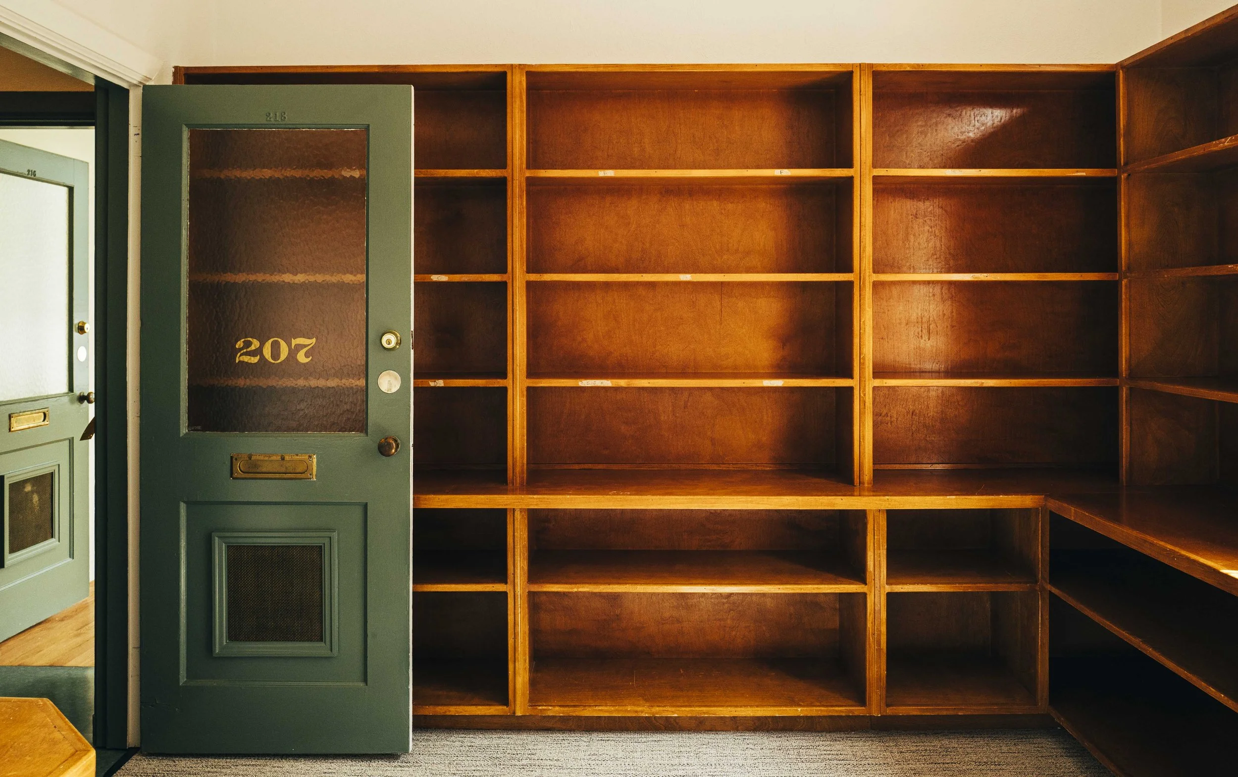 Empty wooden apartment storage shelves with a green door labeled 207, located inside a residential building.