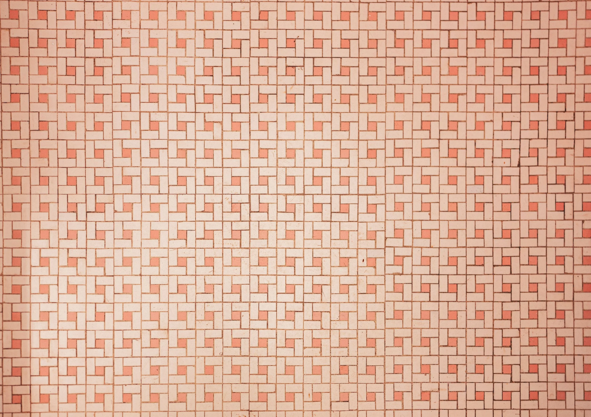 Close-up of a patterned wall with small, square and rectangular pinkish-orange tiles arranged in a repeating geometric pattern.