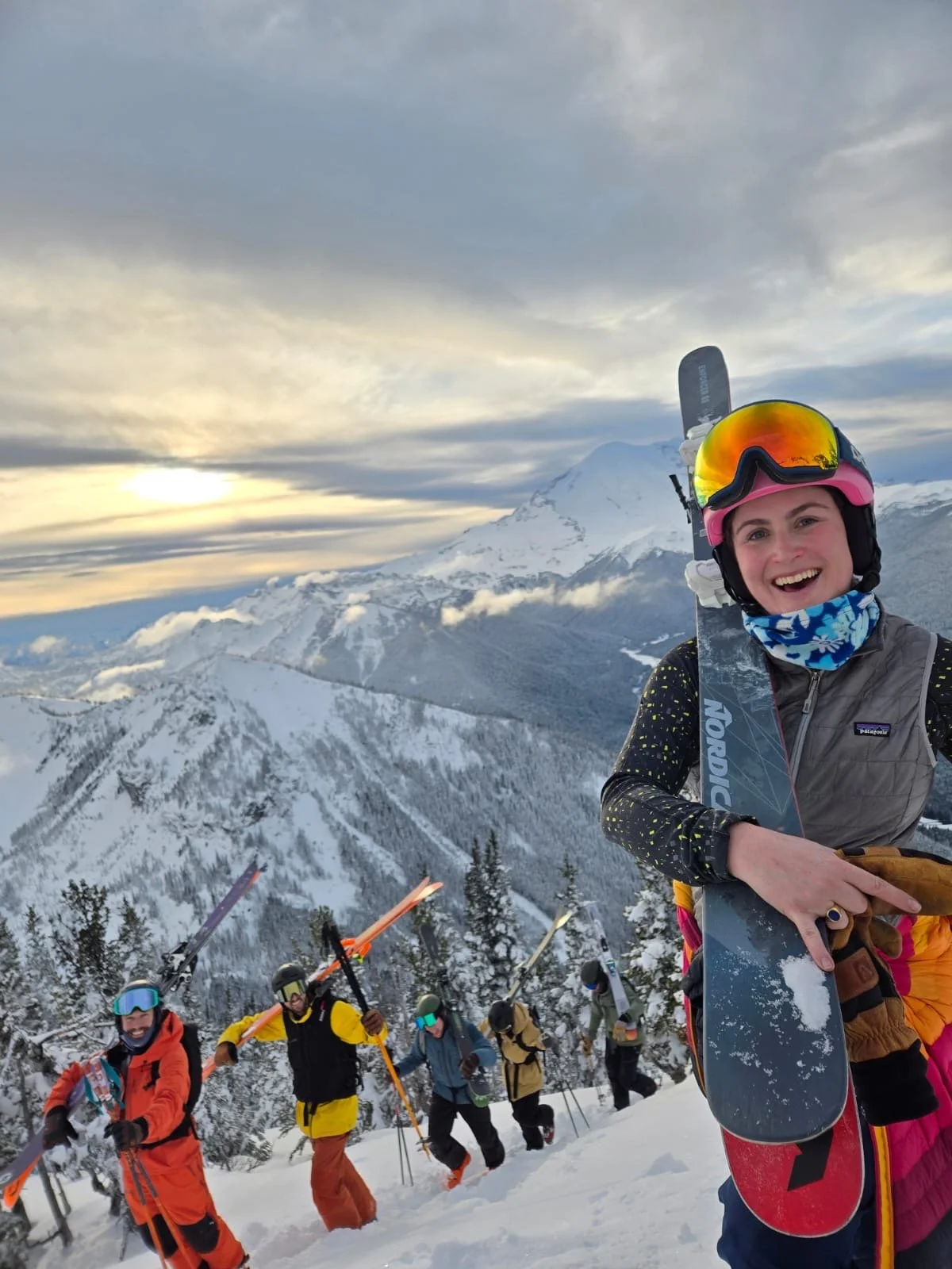 Group of skiers hiking up snowy mountain trail with snow-covered trees and Mount Rainer in the background.