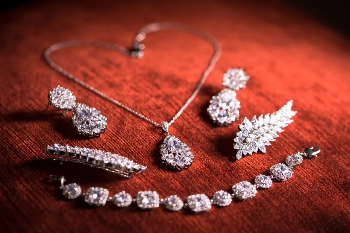 A collection of sparkling diamond jewelry including a necklace, earrings, a bracelet, and a ring arranged on a red fabric background.