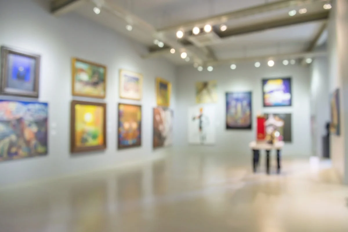 Blurred view of an art gallery with paintings on the white walls and a table in the center.