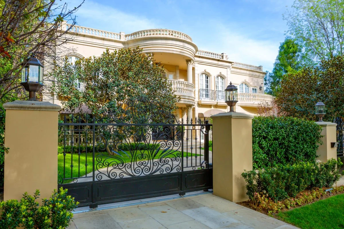 Luxury house with ornate wrought iron gate and lush greenery in front yard.