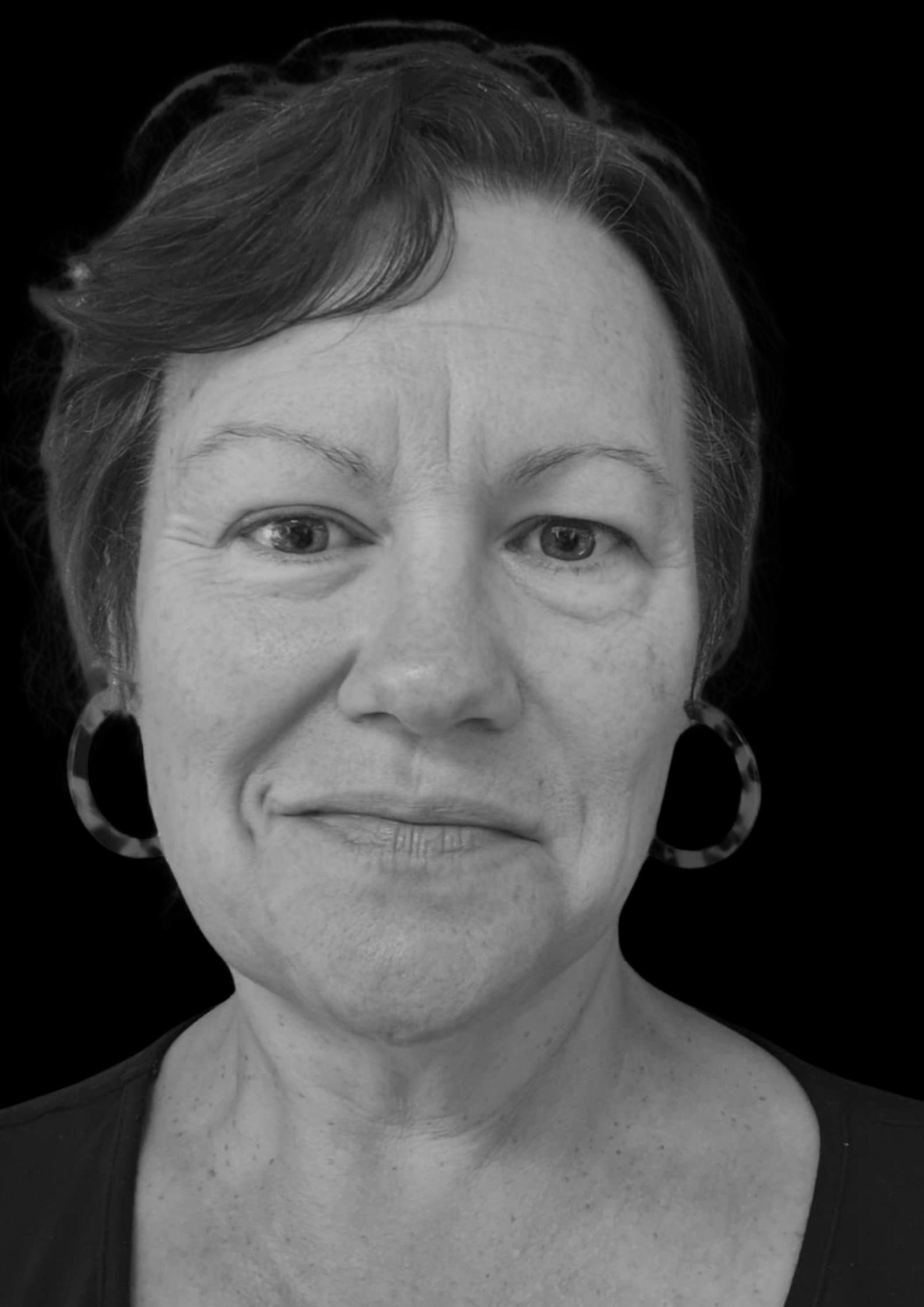 Close-up black-and-white portrait of a woman with short hair, hoop earrings, and wearing a dark top, against a black background.