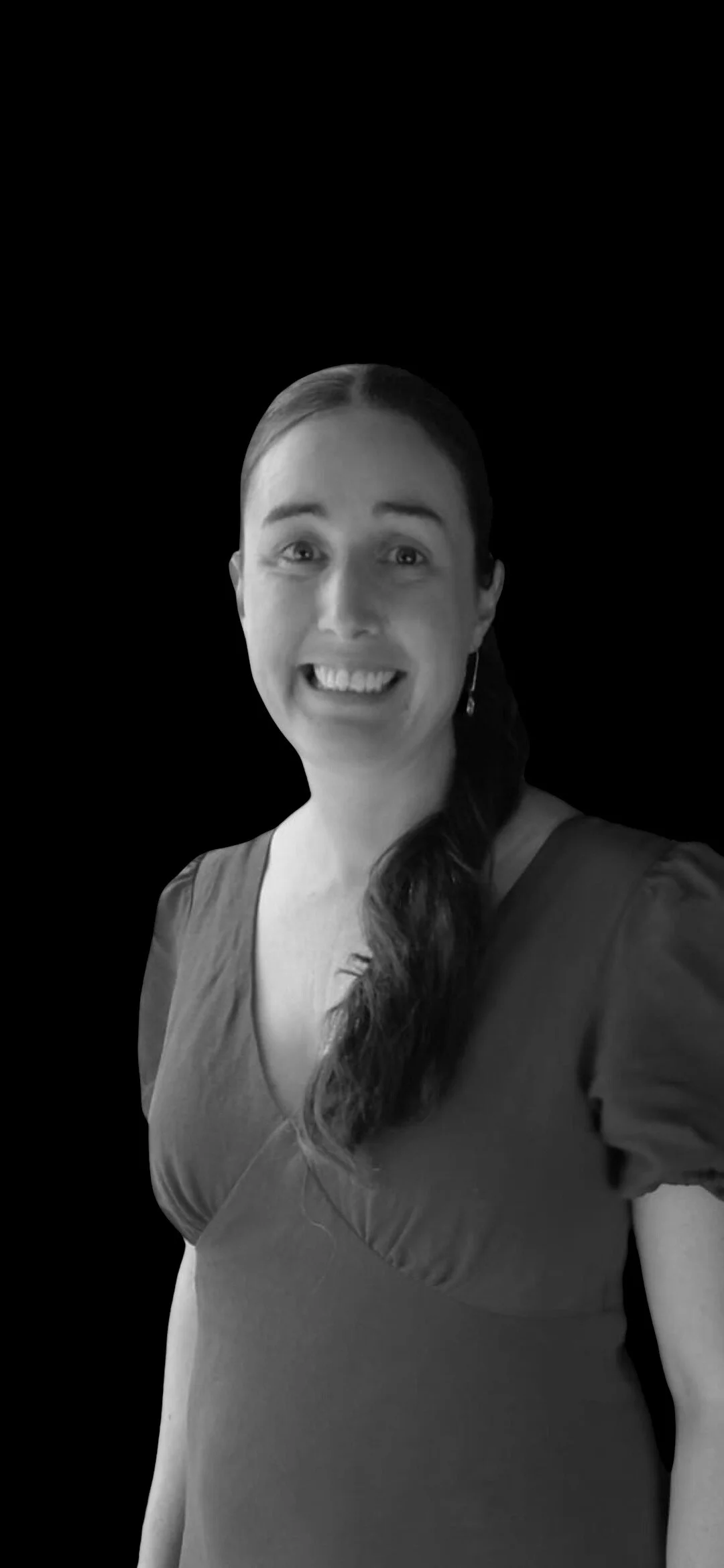A smiling woman with long hair styled in a side ponytail, wearing a short-sleeved top, set against a black background.