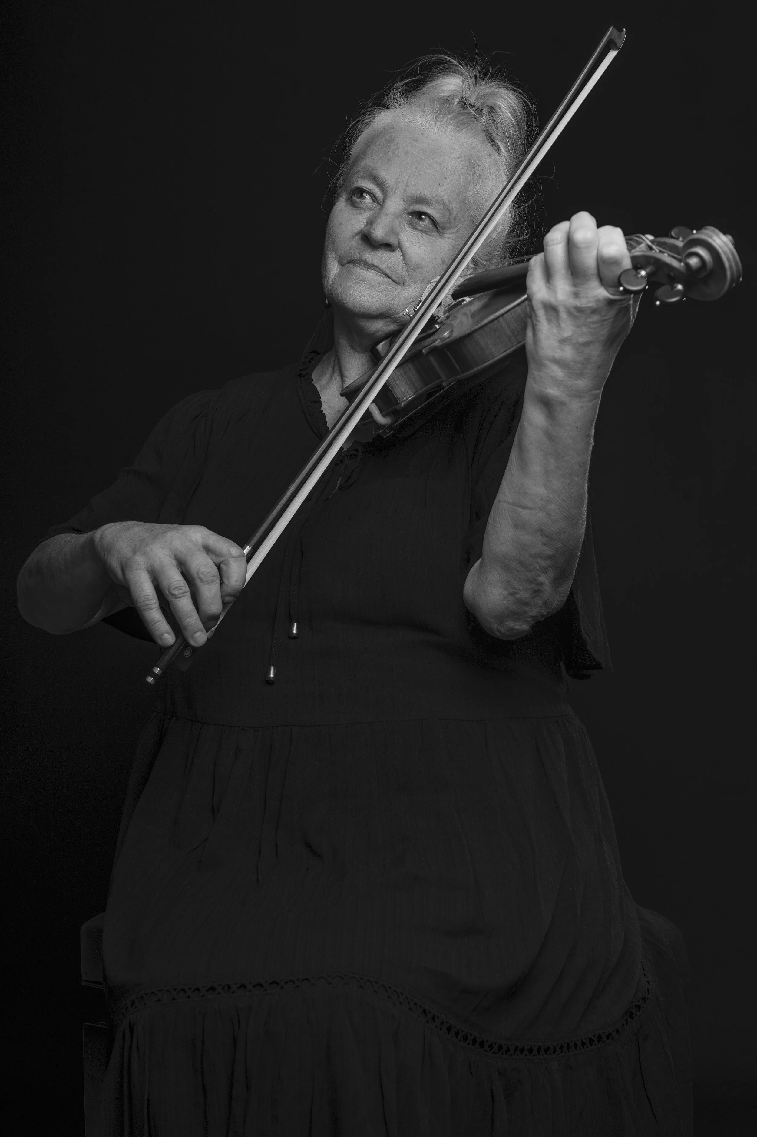 A woman with grey hair playing a violin against a black background.