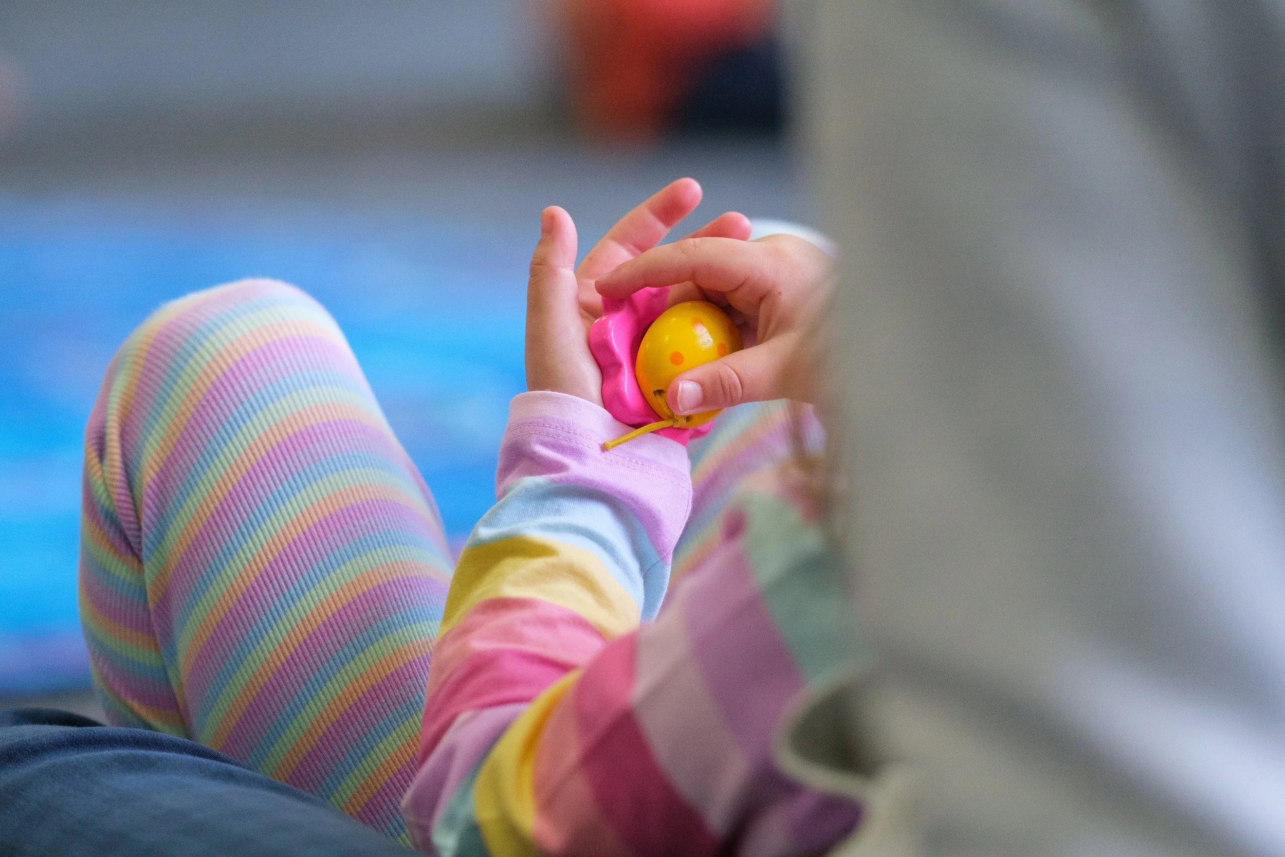 A person in colorful, rainbow-striped pajamas sitting cross-legged, holding a yellow toy with pink accents.
