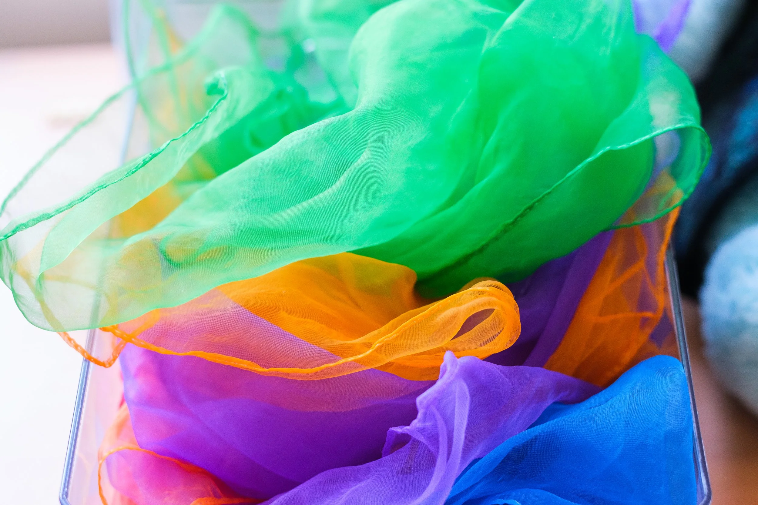 Colorful, crumpled scarves in green, yellow, orange, purple, and blue, inside a clear container.