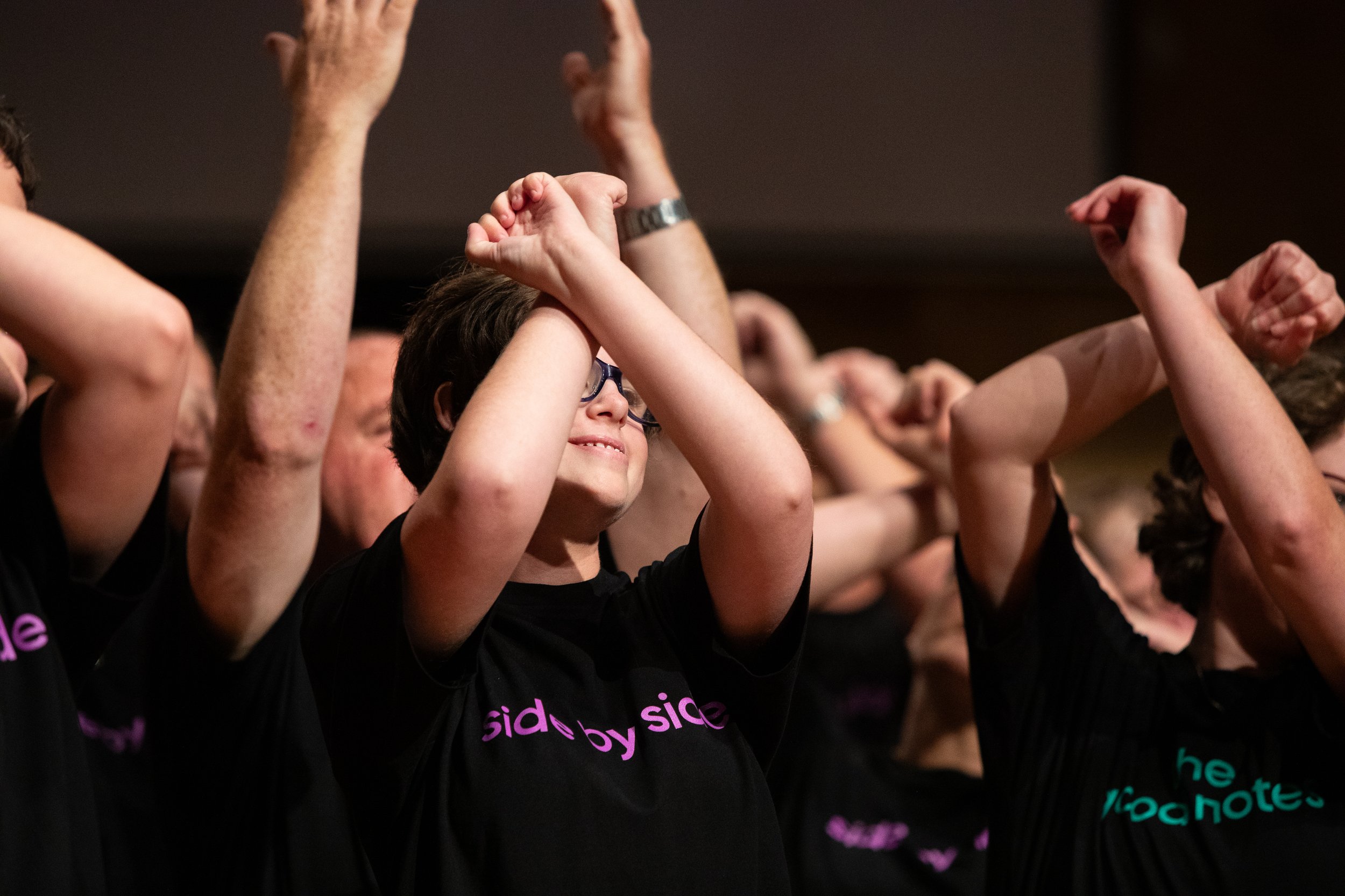 Group of people in black t-shirts participating in an event or activity, raising their arms with fists, smiling and appearing to be engaged and happy.