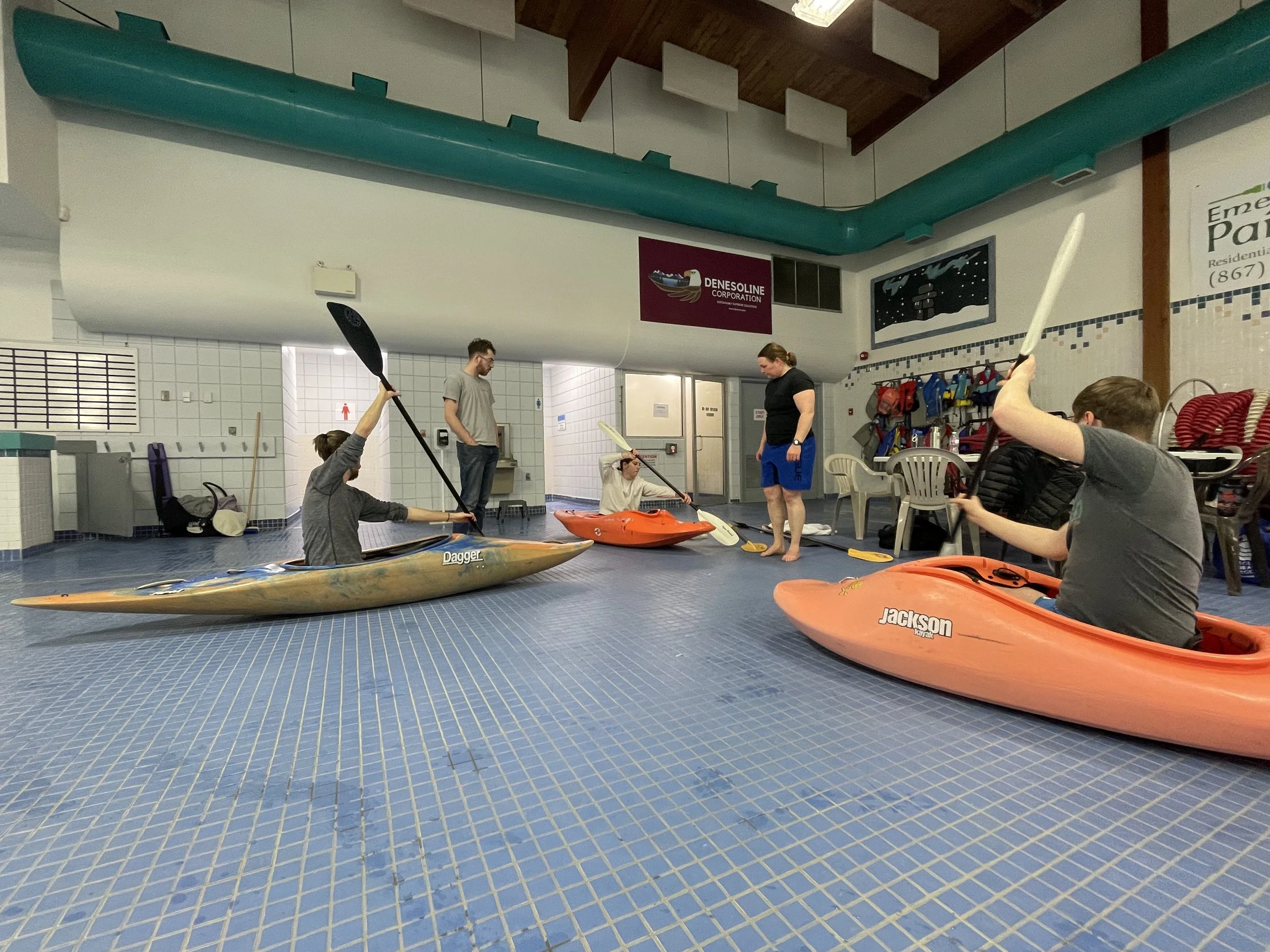 Indoor kayaking lesson with five people in kayaks, two instructors.
