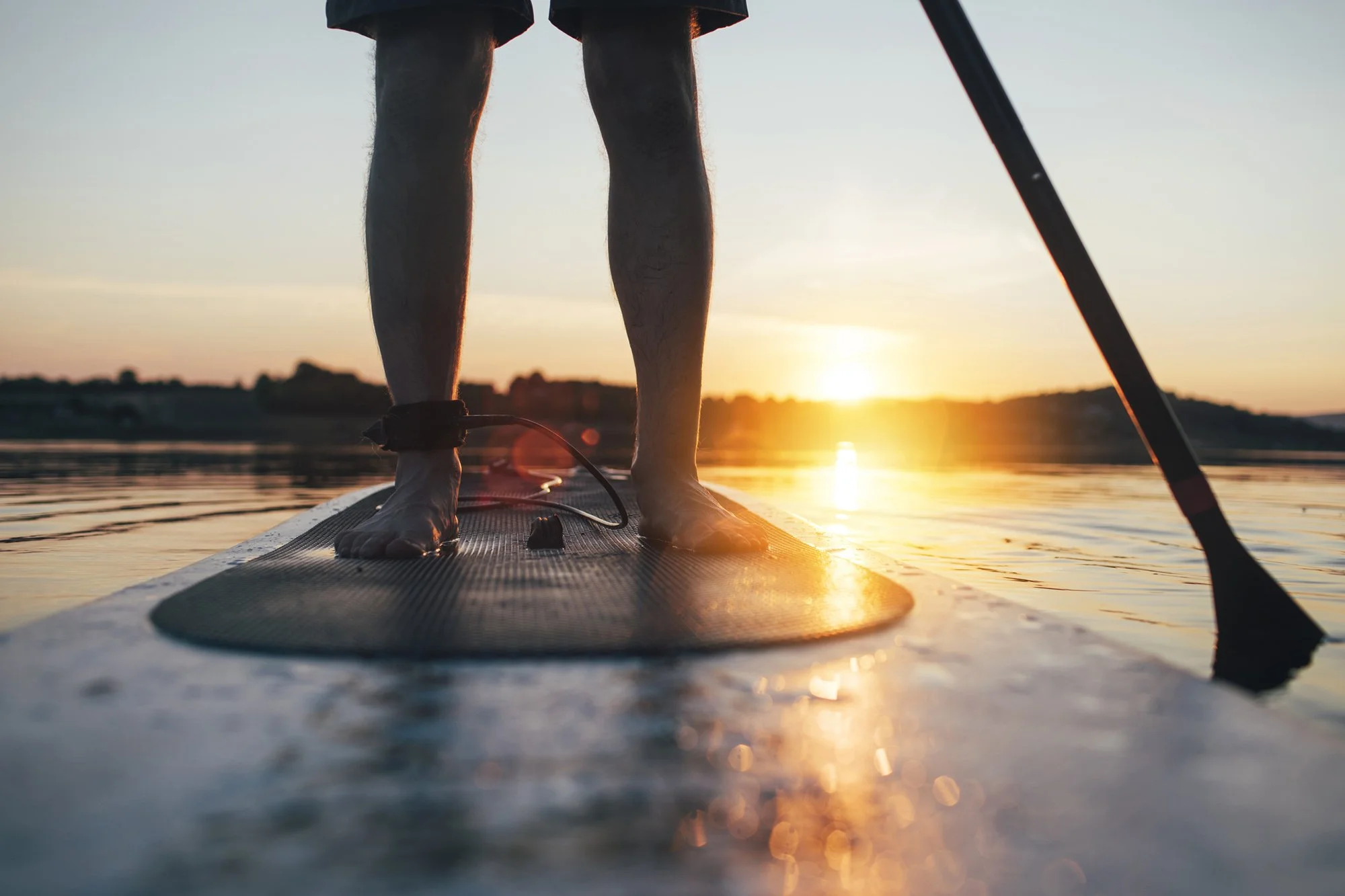 Person standing on a paddleboard at sunset, holding a paddle on calm water.