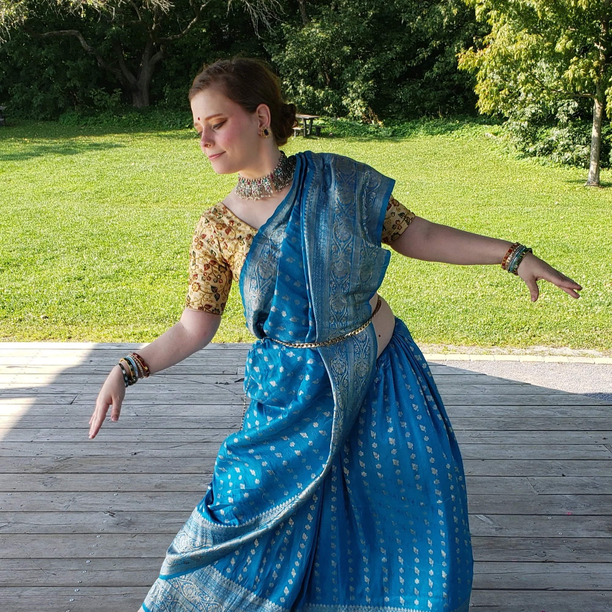 Une femme dans un sari bleu et une blouse dorée dans une pose classique du bharatanatyam