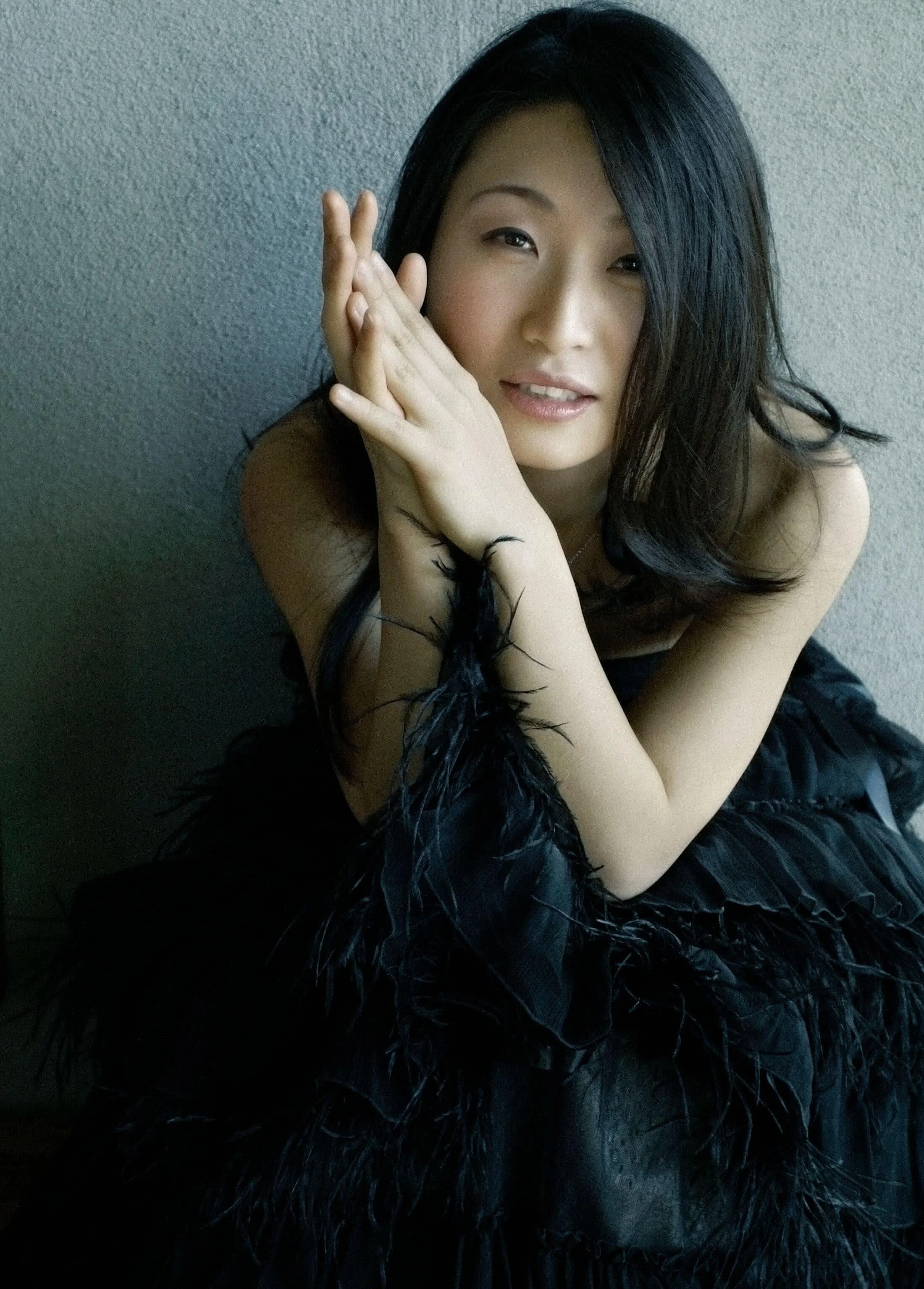 Portrait of pianist Soyeon Kate Lee resting her hands near her face against a textured gray background.