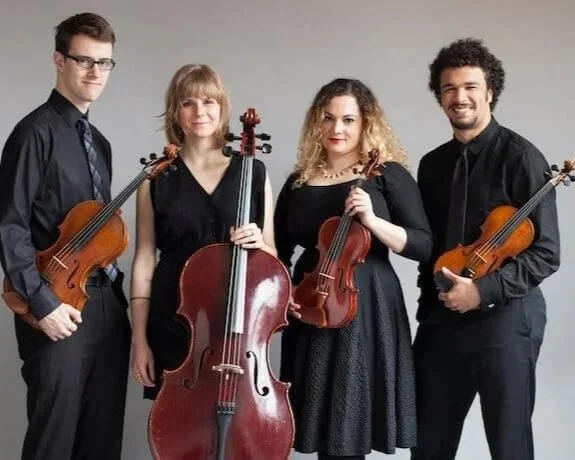 Four string musicians in PUBLIQuartet posing with violin, viola, and cello in a studio portrait against a light background.