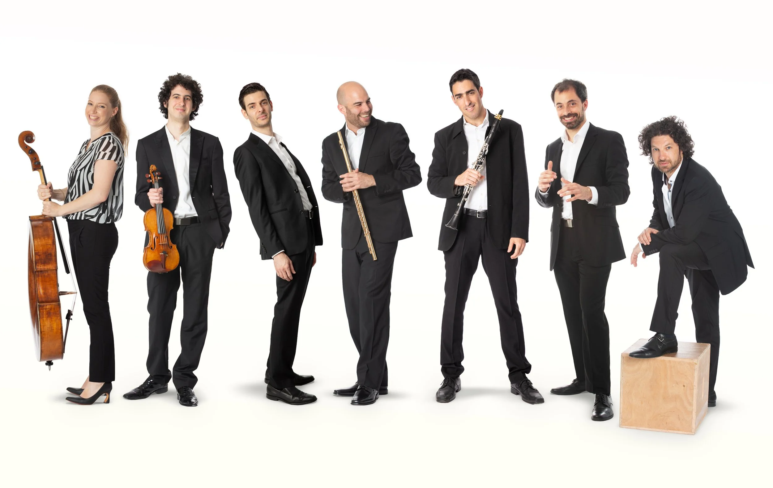 Members of the Israeli Chamber Project posing with string and wind instruments against a white background.