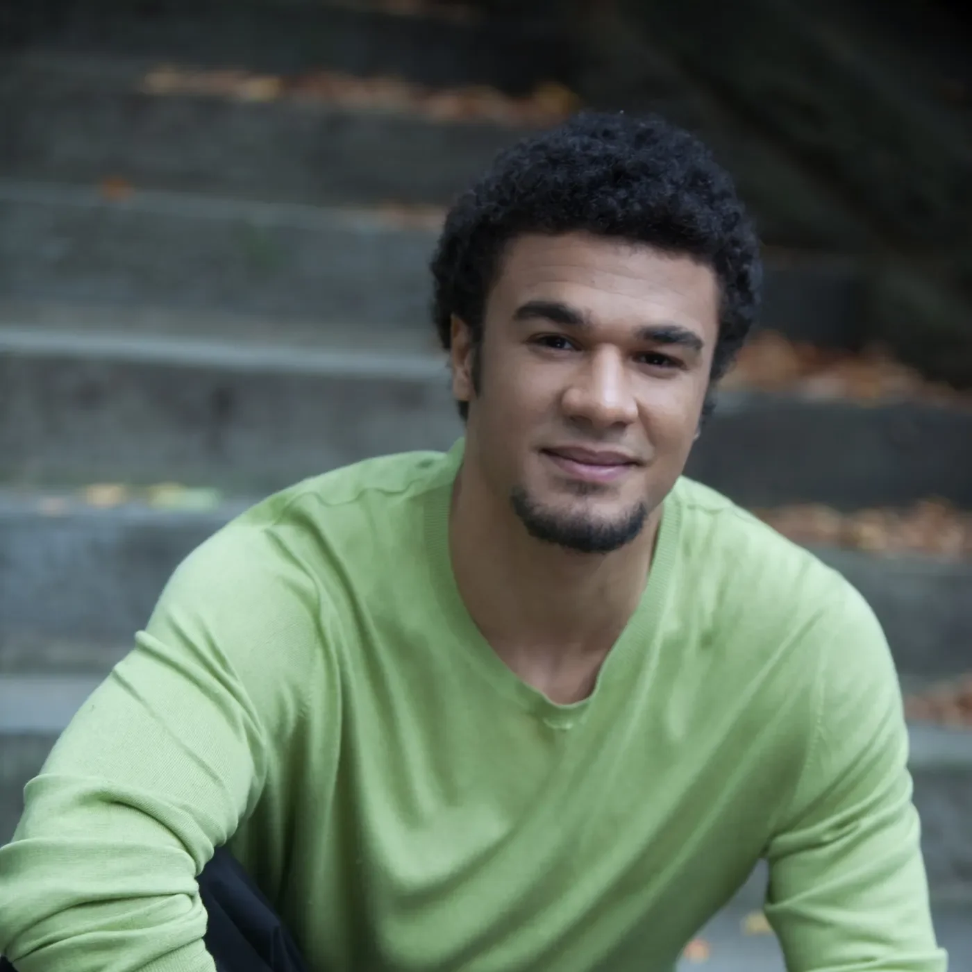 Portrait of Curtis Stewart in a green shirt outdoors on stone steps.