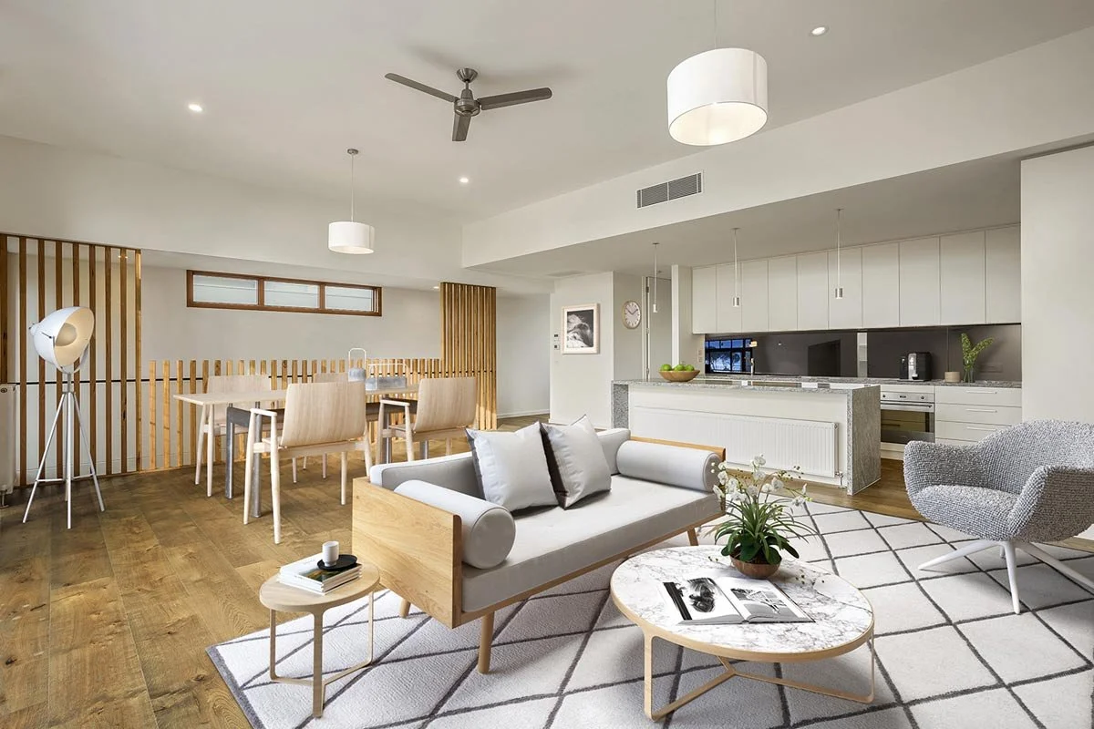 Modern open-concept living and dining area with wooden flooring, white walls, a white sofa, a marble coffee table with a plant, a grey accent chair, dining table with four chairs, pendant lights, and a contemporary kitchen in the background.