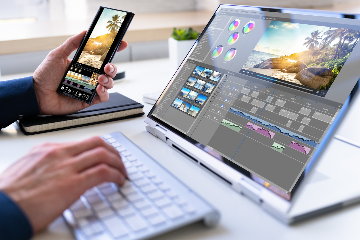 Person editing a video project on a laptop with a timeline and multiple video clips, while another hand holds a smartphone with a photo of a beach scene.