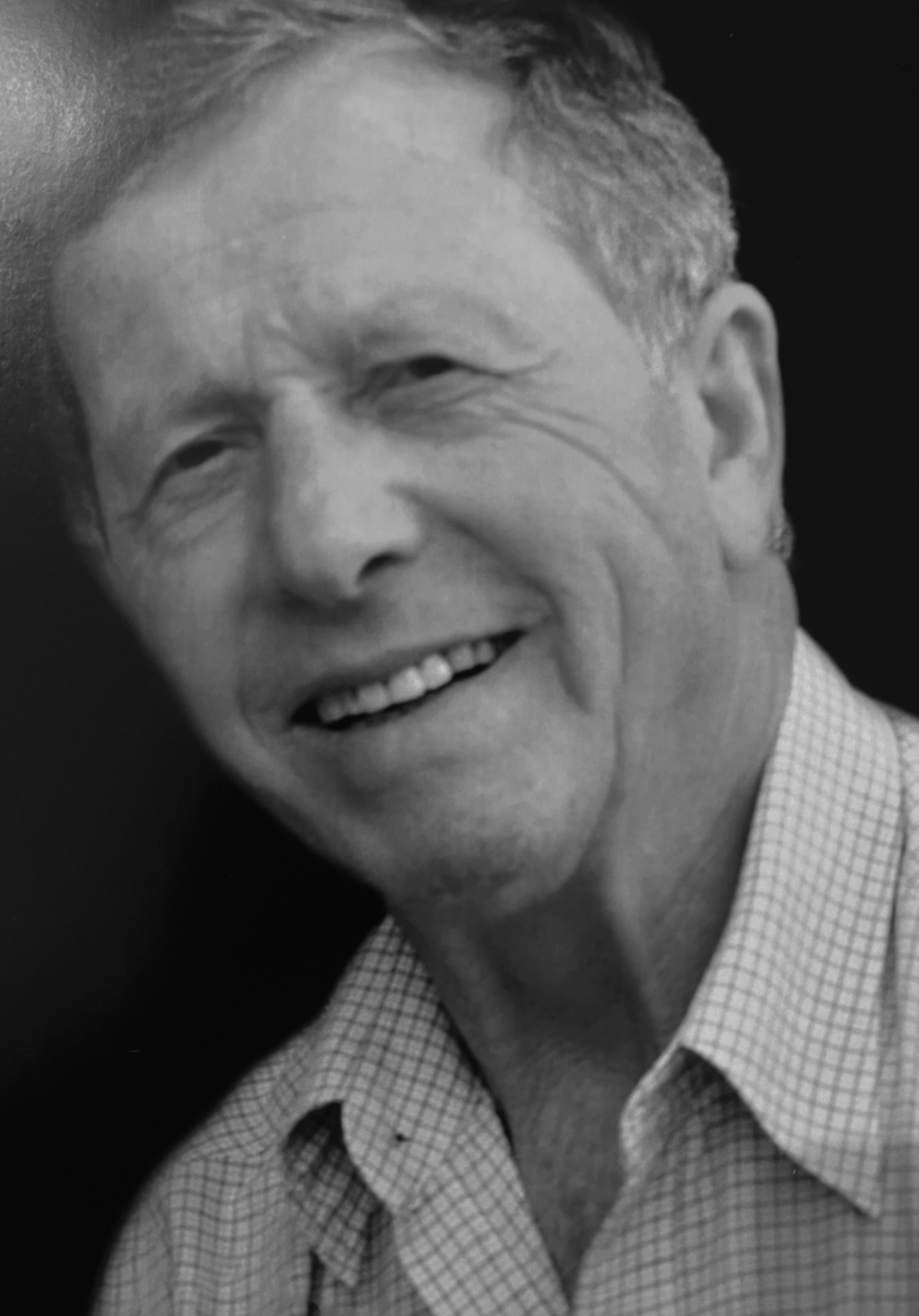 A smiling middle-aged man with short, light-colored hair wearing a checkered shirt.