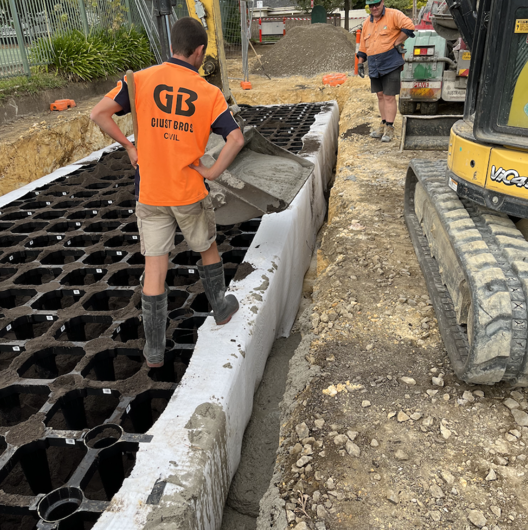 Construction workers pouring concrete onto a grid of plastic or metal forms for a sidewalk or foundation at a construction site.